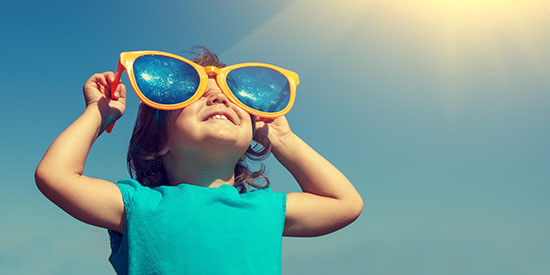 Vrolijk klein meisje dat naar de zon kijkt met een grote zonnebril